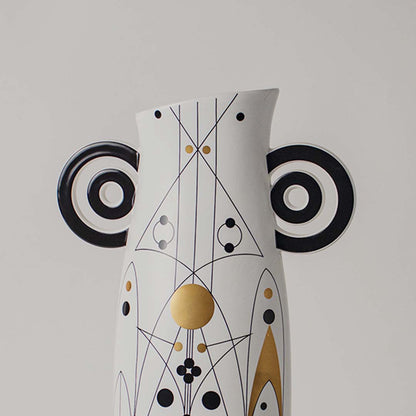 Closeup of white abstract ceramic vase showing black and gold geometric detailing and sculptural circular side handles.