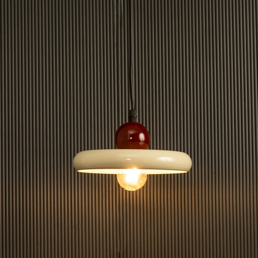 White circular pendant with red top glowing warmly on a dark background emphasizing its clean lines and balanced form.