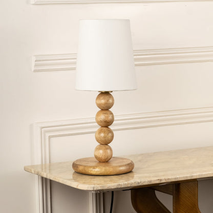 Natural wood table lamp with sculpted bead base and white fabric shade for warm organic interior decor styling.