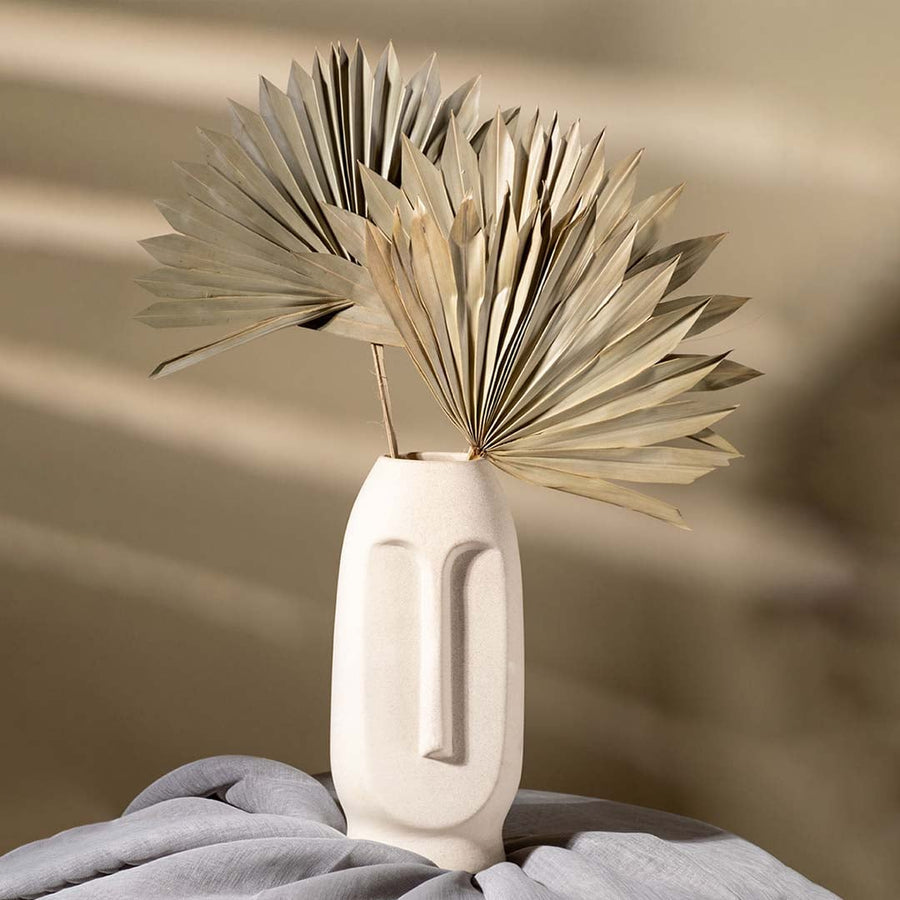 Textured beige ceramic face vase with carved facial details and dried palm leaves adding a natural artistic touch to warm minimal interiors.
