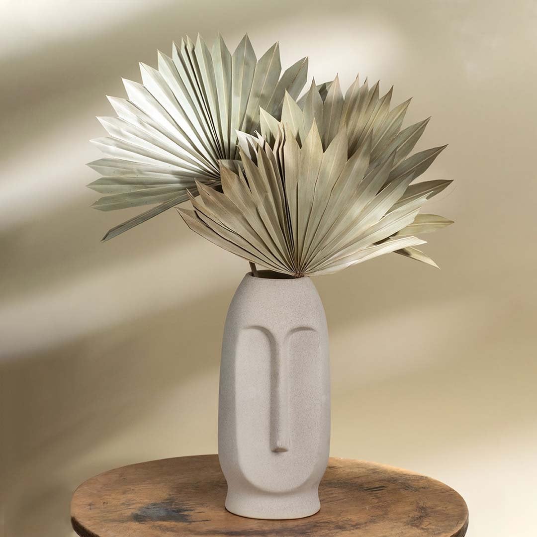 Beige ceramic face vase with sculpted minimalist features styled with dried fan palm leaves creating an earthy modern accent for contemporary decor.