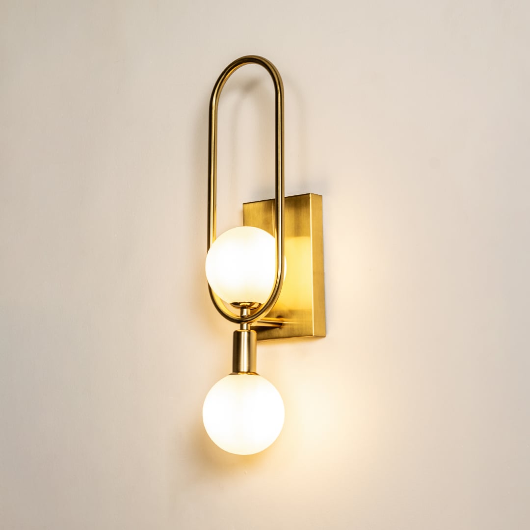 A double globe metal wall light with gold framing mounted on a beige wall creating soft warm lighting and enhancing luxurious contemporary décor.