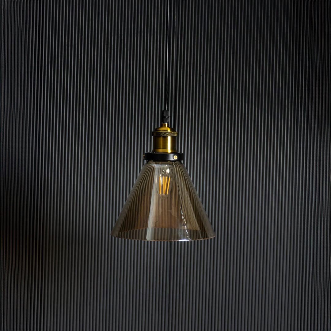 Amber glass pendant light with bulb off on black background featuring brass and black metal fitting design.