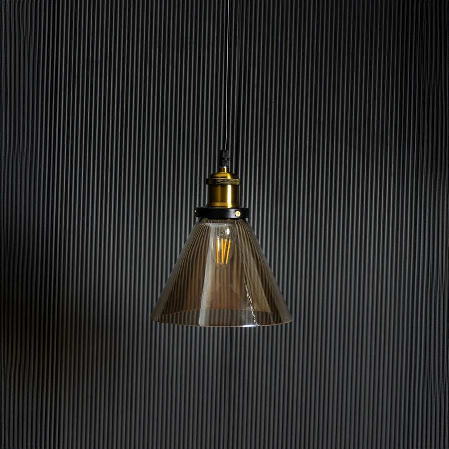 Amber glass pendant light with bulb off on black background featuring brass and black metal fitting design.