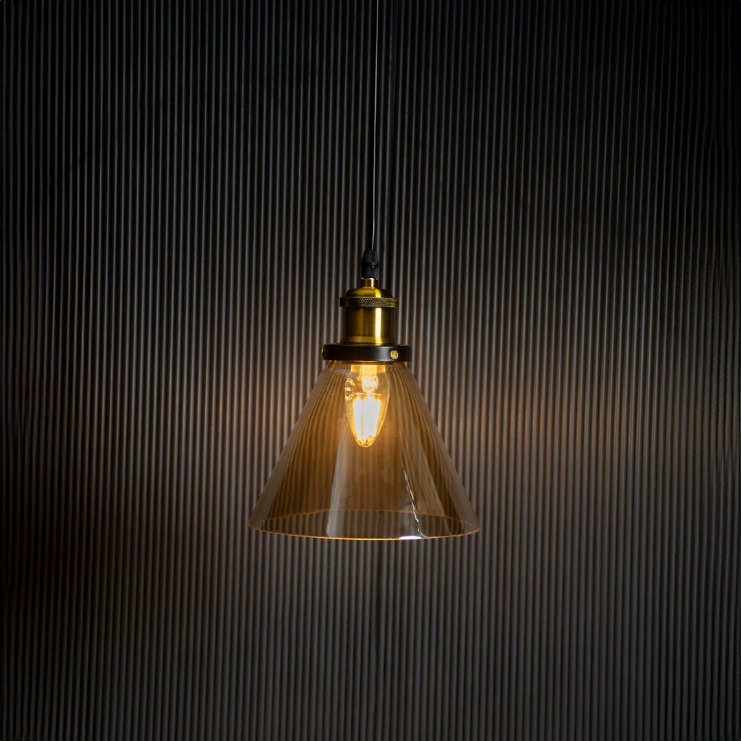 Amber glass pendant light glowing on black background with brass and black metal fitting for stylish home decor.