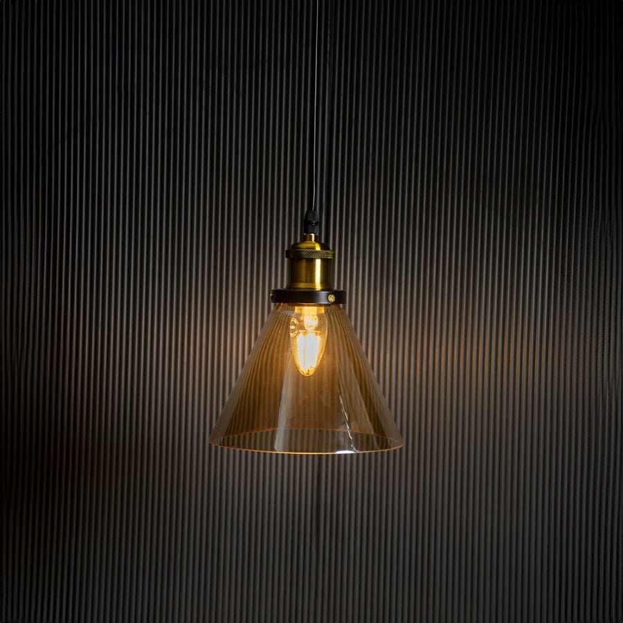 Amber glass pendant light glowing on black background with brass and black metal fitting for stylish home decor.
