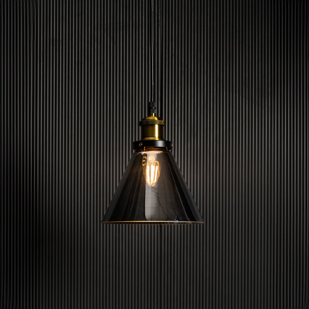 Smokey glass pendant light glowing on black background with elegant brass and black fitting for home interiors.