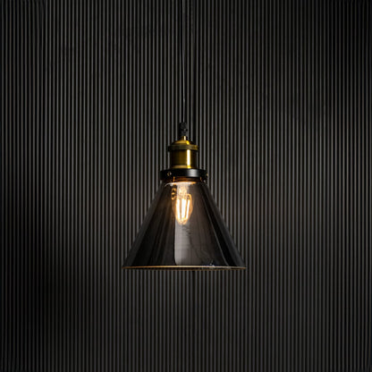 Smokey glass pendant light glowing on black background with elegant brass and black fitting for home interiors.