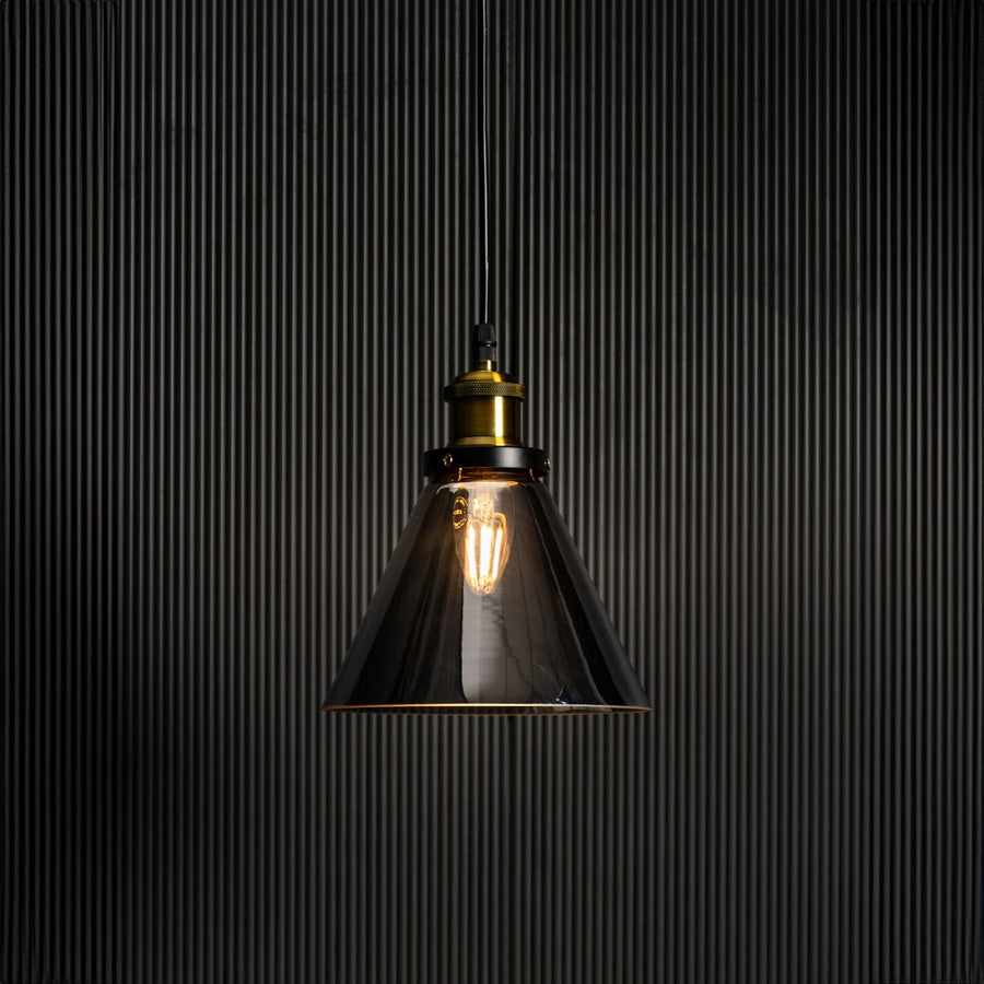 Smokey glass pendant light glowing on black background with elegant brass and black fitting for home interiors.
