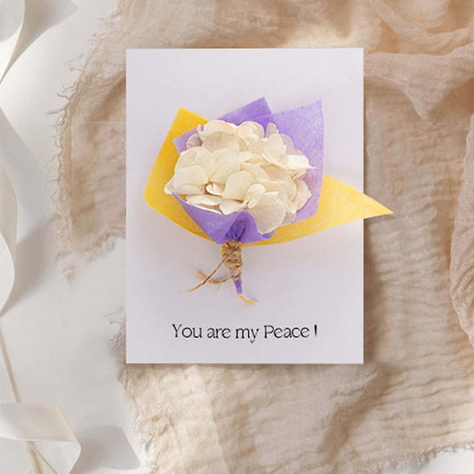 Greeting card with ivory paper flower bouquet wrapped in purple and yellow paper displayed on white background.
