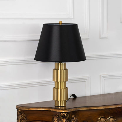 Modern table lamp with golden cylindrical base and black lampshade turned off on white background decor.