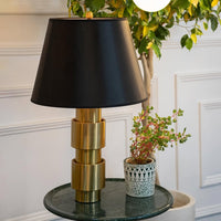 Elegant gold base table lamp with black shade styled on side table with plants for luxury home decor.