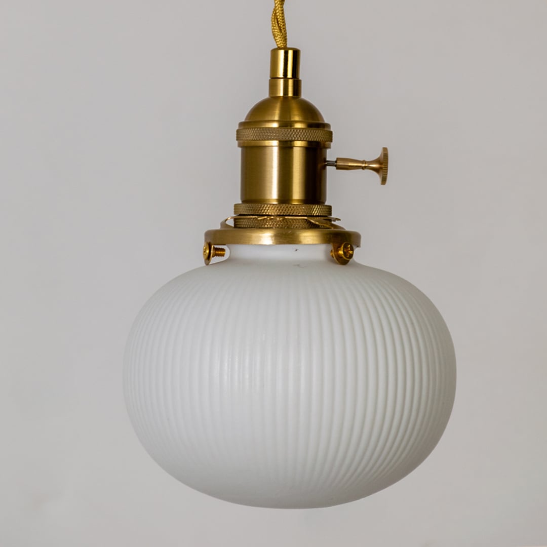 Closeup of round ribbed white glass pendant light showing textured globe shade and gold metal holder for elegant home decor.