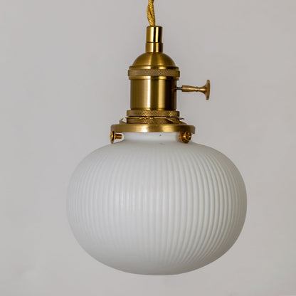 Closeup of round ribbed white glass pendant light showing textured globe shade and gold metal holder for elegant home decor.