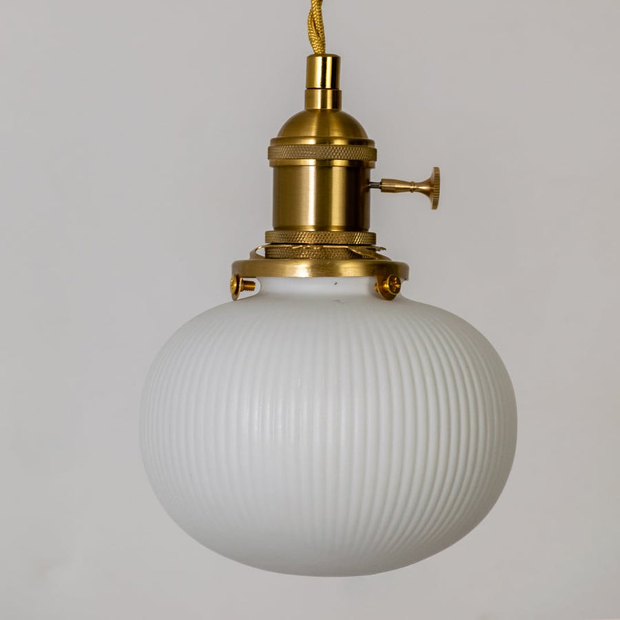 Closeup of round ribbed white glass pendant light showing textured globe shade and gold metal holder for elegant home decor.