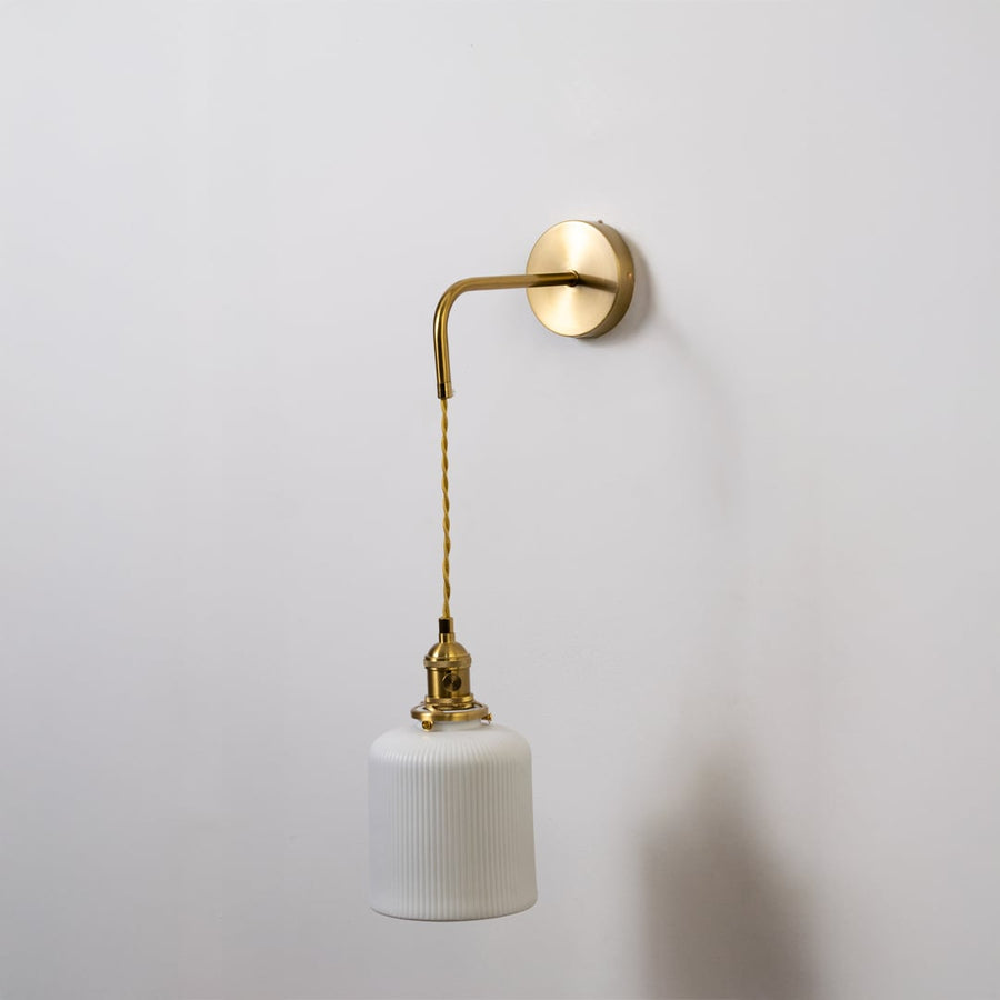 Gold metal wall light with white ribbed cylinder shade shown switched off on white background for minimal stylish decor.