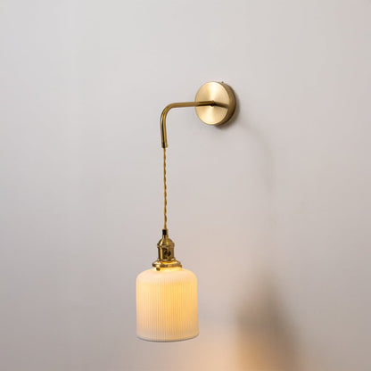 Gold metal wall light with white ribbed cylinder shade glowing softly on white background for elegant modern home decor.