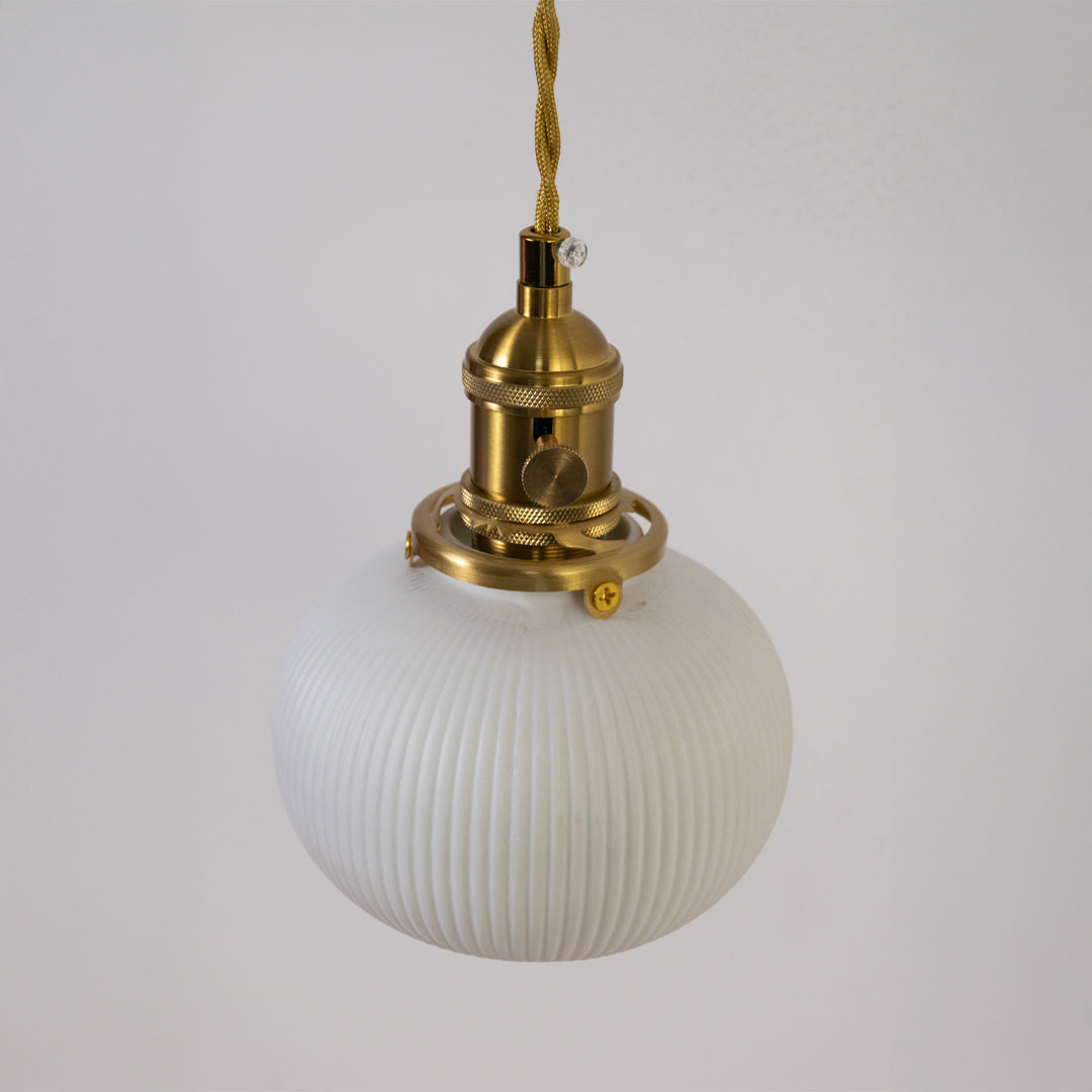 Closeup pendant light in gold metal finish with ribbed glass globe for kitchen or dining decor lighting white background.