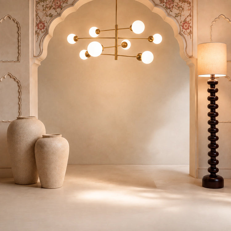 A modern multi-light chandelier with spherical frosted glass globes and a brass frame hangs in a warm, cream-colored room with an arched doorway, decorative vases, and a tall dark wooden floor lamp.