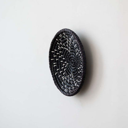 Side view of handwoven black wall basket made of rustic natural fiber with boho style for wall decor.