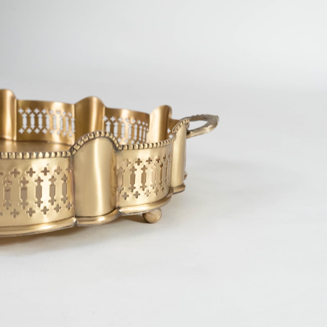 A closeup view of the gold serving tray showing its carved scalloped border intricate pattern detailing and smooth metallic texture with bowls placed inside the design frame.