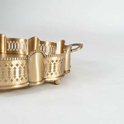 A closeup view of the gold serving tray showing its carved scalloped border intricate pattern detailing and smooth metallic texture with bowls placed inside the design frame.