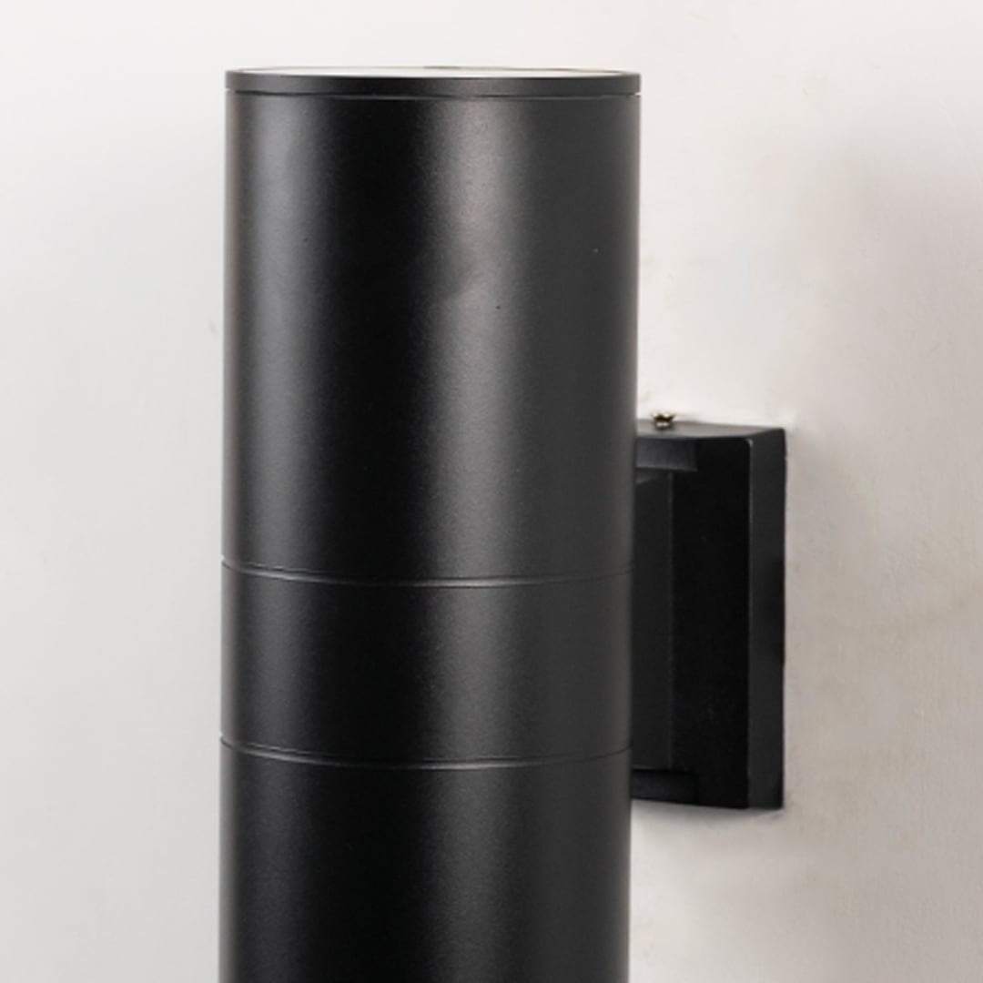 Closeup of tall black metal cylindrical outdoor wall light showing smooth matte finish and modern exterior design.