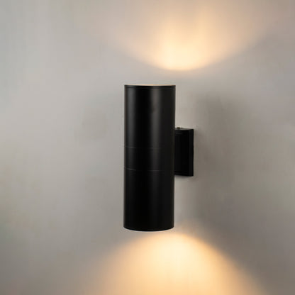 Black metal outdoor wall light glowing on white wall for elegant modern patio and entryway lighting decor.