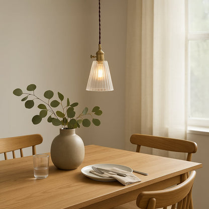 Clear ribbed glass pendant light with brass holder hanging above table adding warm glow to modern dining interiors.
