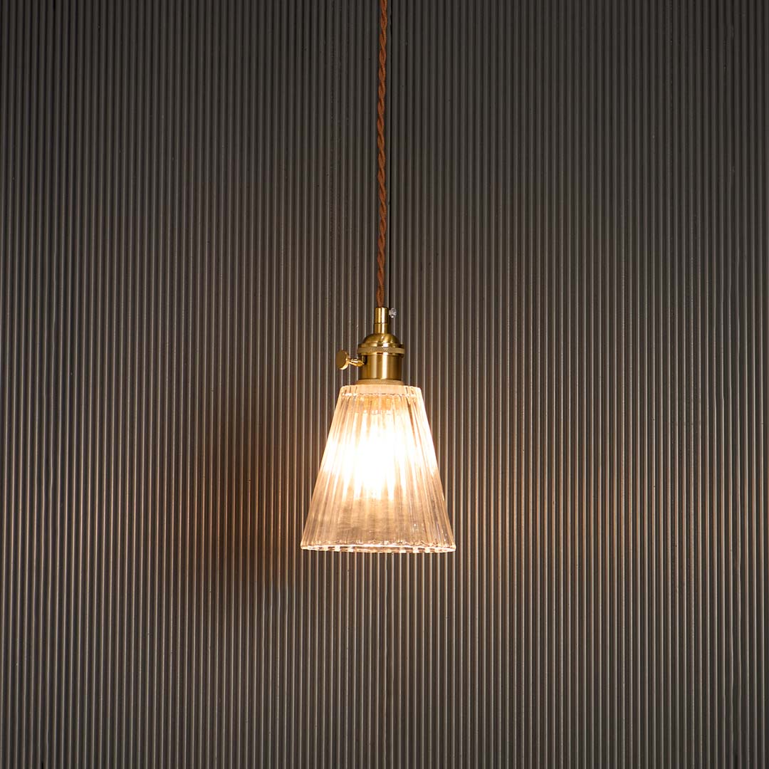 Clear glass cone pendant light glowing warmly with brass holder against black background for elegant room ambience.