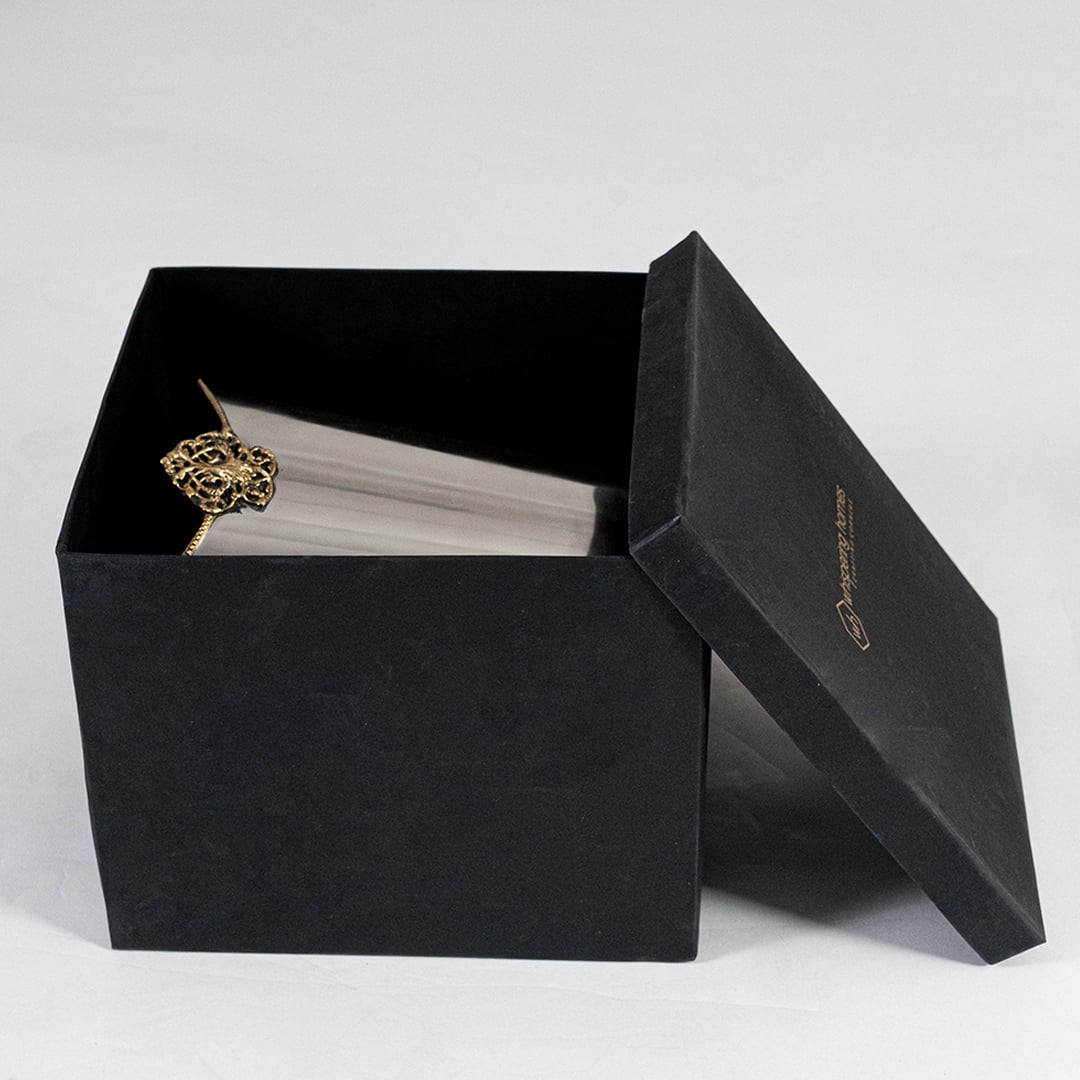 Silver waste bin with gold detail partially packed in black branded box with open lid for elegant gift-ready display.