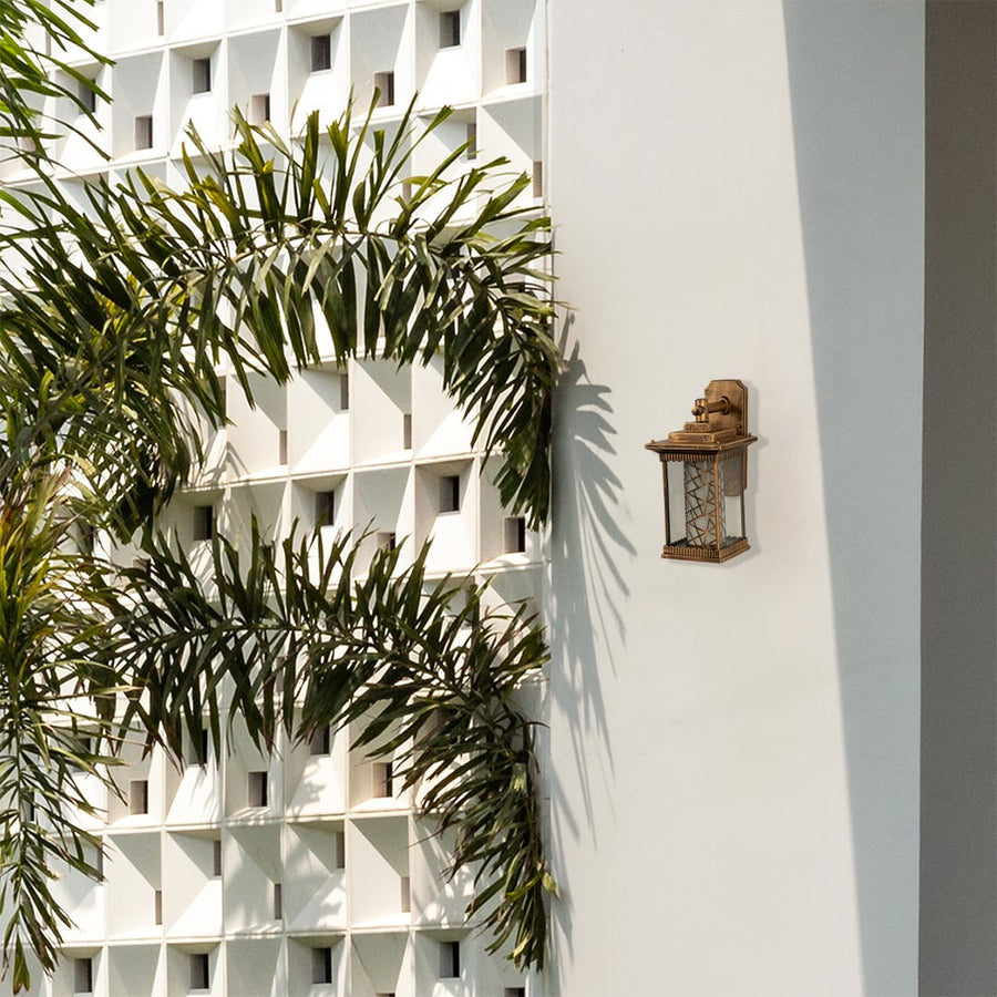 Gold metal outdoor wall lantern with patterned glass displayed on a modern white exterior wall with greenery adding refined outdoor decor styling.