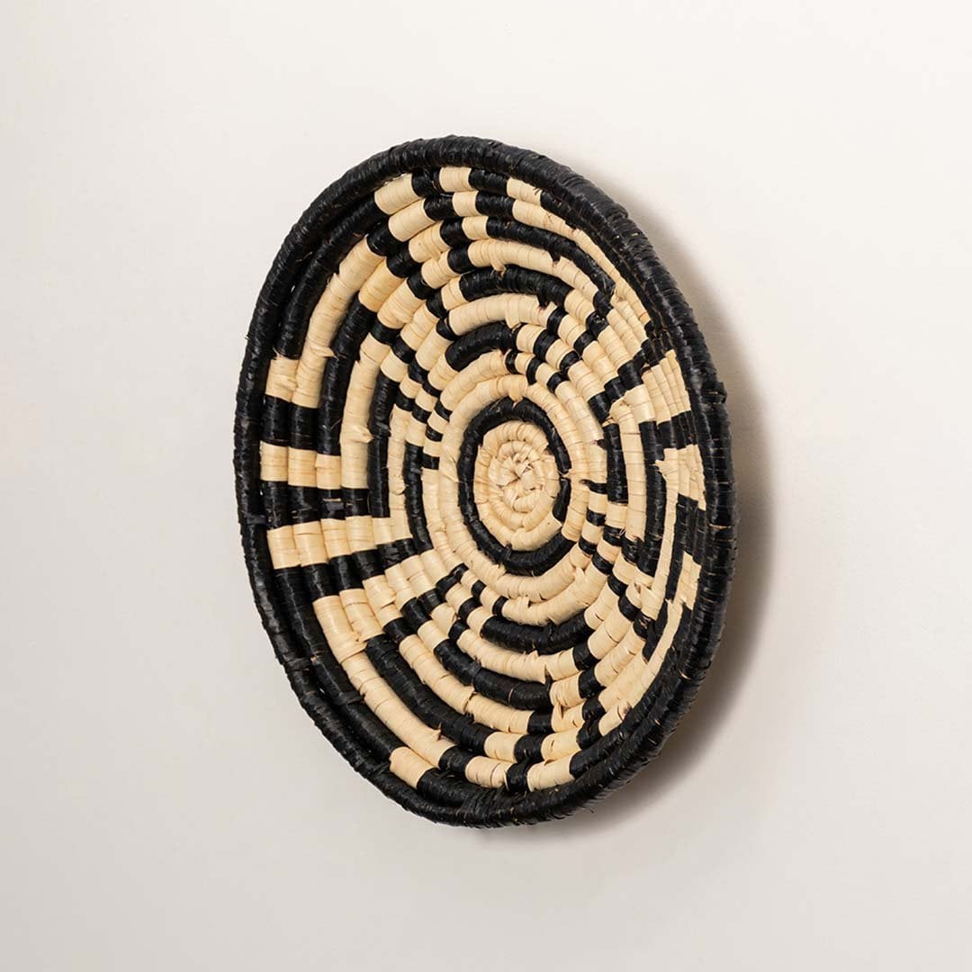 Side profile of the flat woven wall basket showing the thick natural fiber coils and black wrapping details on a white surface for quality.