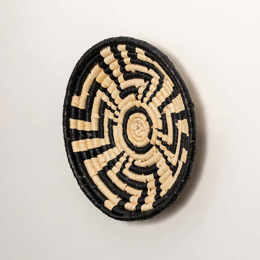 Side profile of the flat woven wall basket showing the thick natural fiber coils and black wrapping details on a white surface for quality.