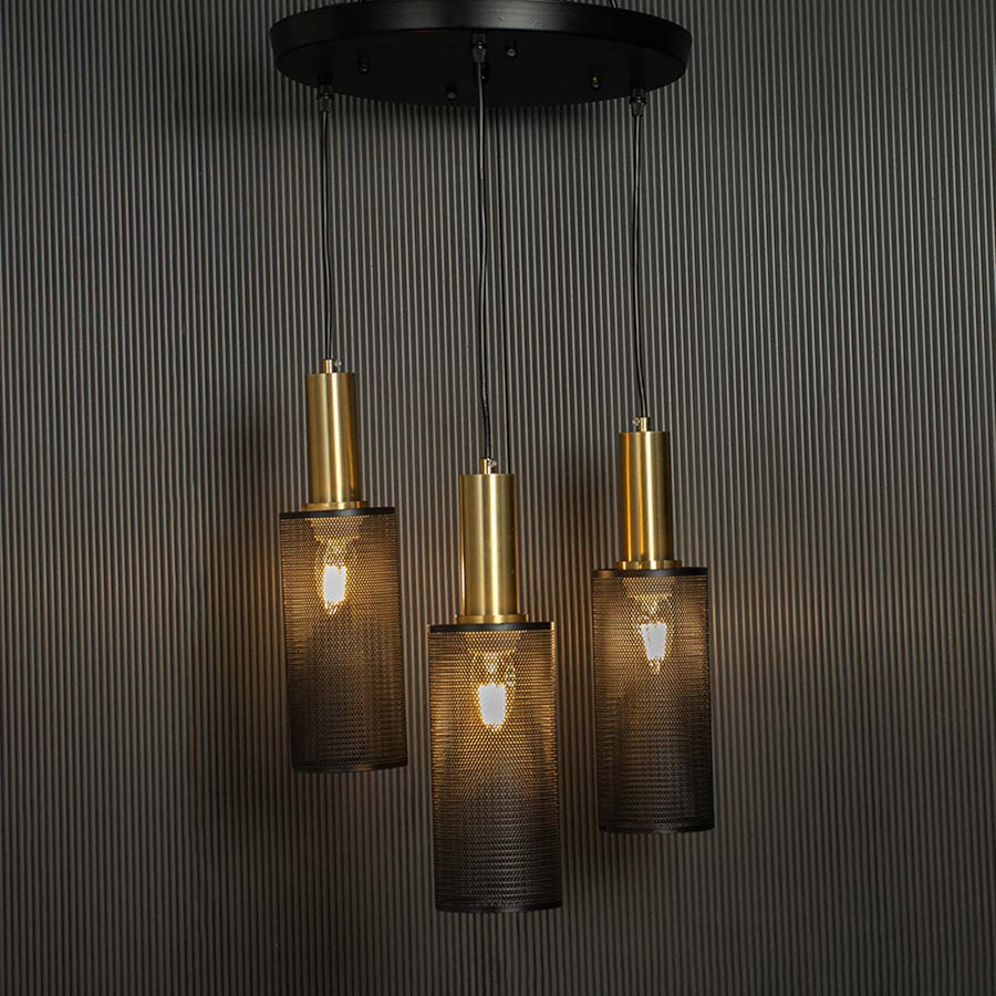 Triple mesh pendant light with gold fittings and warm illumination standing out against a dark black backdrop with its perforated metal shades.