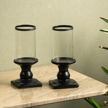 Set of black metal candle holders with clear glass hurricanes placed on a marble surface for elegant decor.