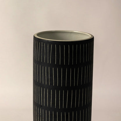 Closeup of black ceramic vase with detailed white stripe design and orange accent showing fine texture for home decoration.
