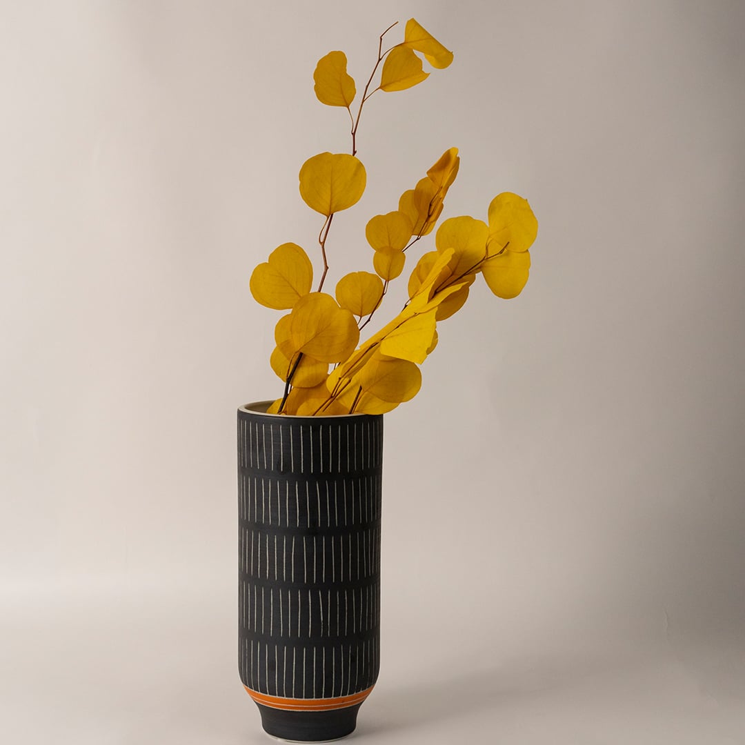Stylish black ceramic vase with vertical white stripes and orange base accent adding elegance to modern living room decor.