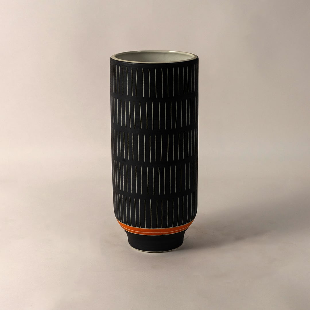 Contemporary black ceramic striped vase with orange detail styled for home interior decoration on simple white background.