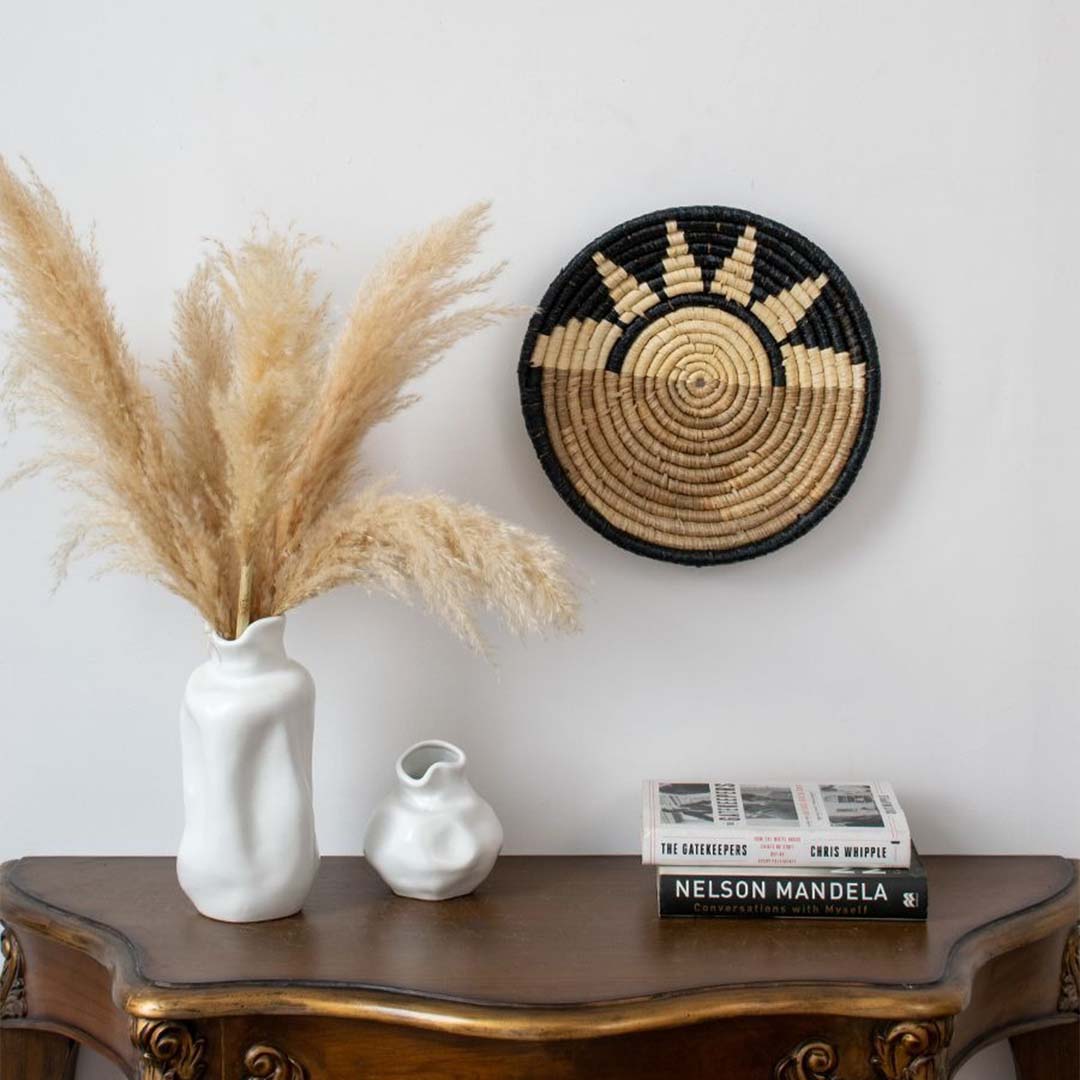 Black and beige bamboo wall plate styled above wooden table with white vases adding earthy charm to home interior.