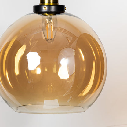 Amber glass globe pendant light with brass metal fixture showcasing glossy finish and warm modern lighting style.
