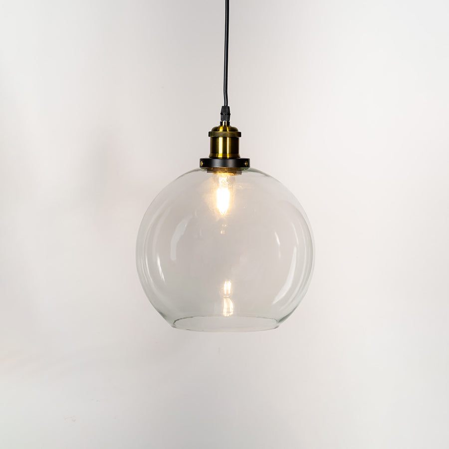Clear glass pendant light with brass finish metal holder and globe design for elegant modern ceiling lighting decor.
