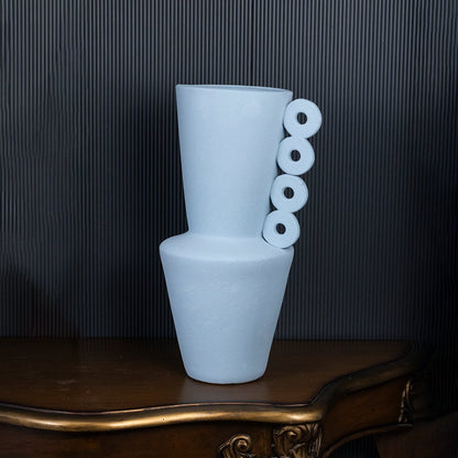 Matte blue vase with artistic circular handles standing on black background displaying modern handcrafted decor style.