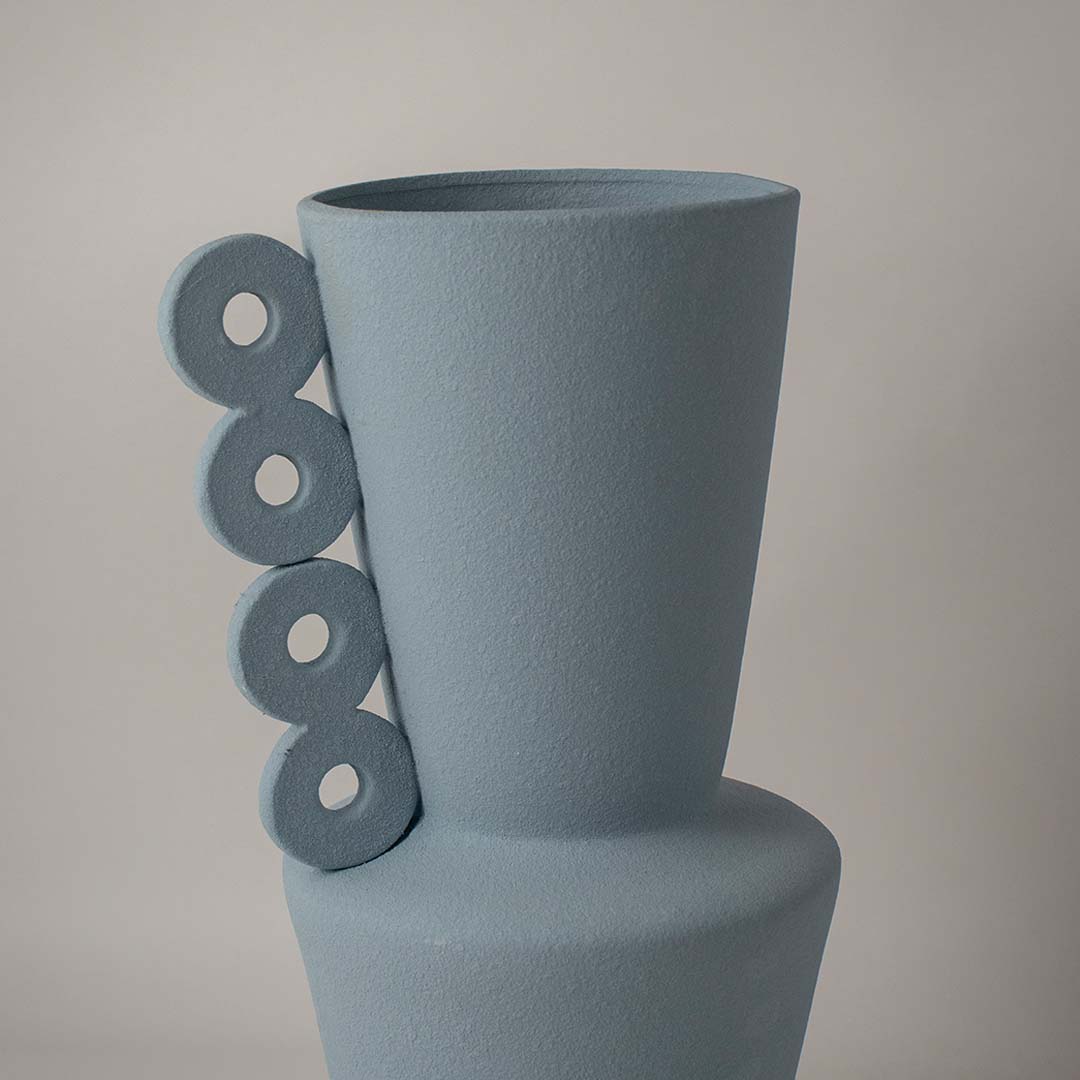Closeup of matte blue ceramic vase showing textured finish and circular ring handles reflecting artistic craftsmanship.