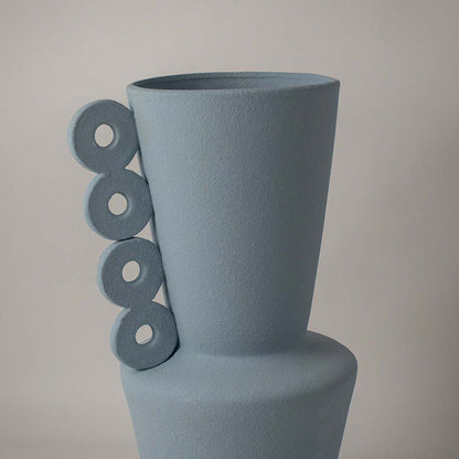 Closeup of matte blue ceramic vase showing textured finish and circular ring handles reflecting artistic craftsmanship.