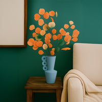 Blue ceramic vase with unique circular handles holding orange and green dried leaves on wooden table beside beige sofa.