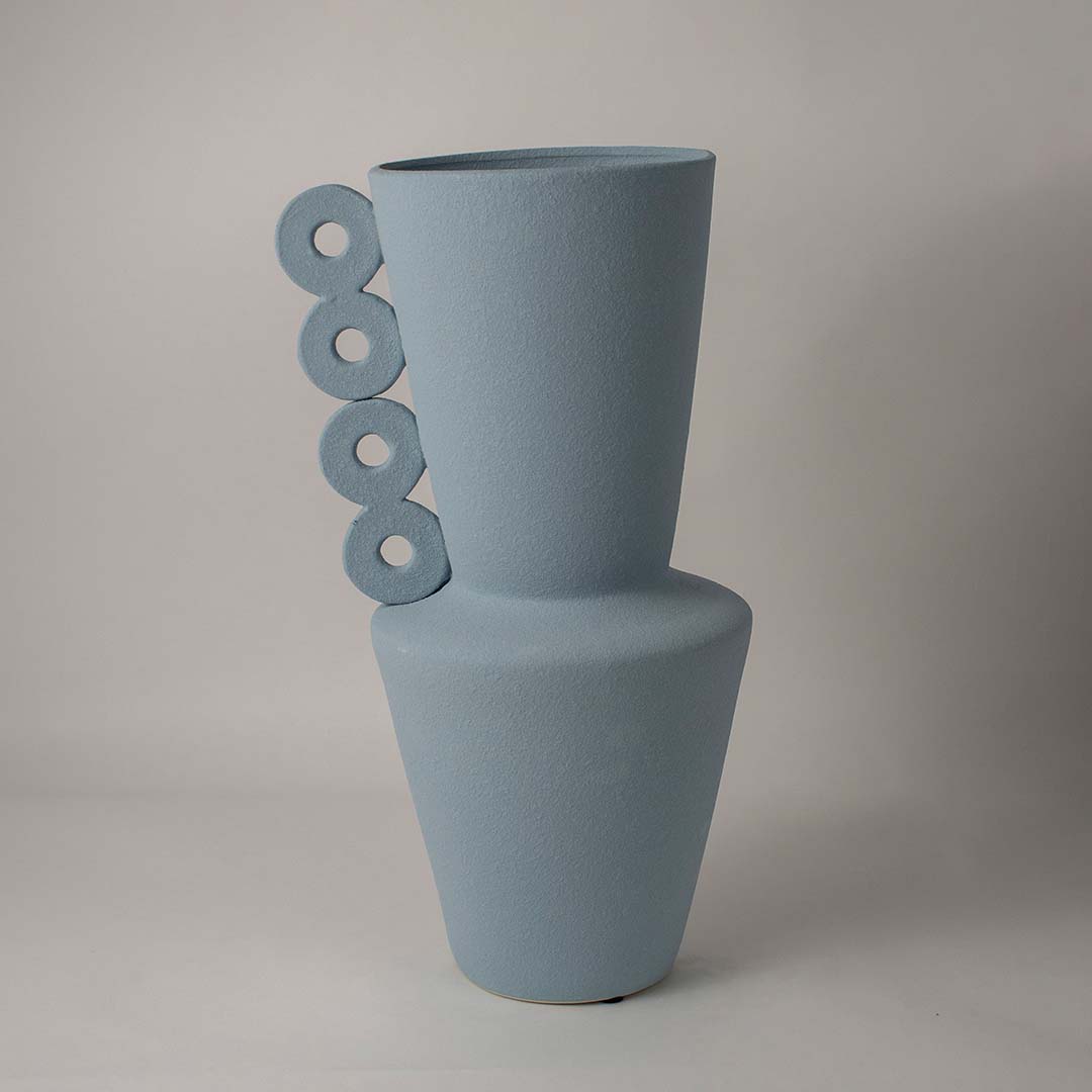 Matte blue ceramic vase with circular side handles on white background showcasing modern artistic home decor design.