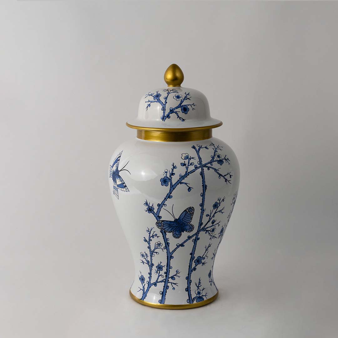 Decorative ceramic jar with blue botanical pattern and gold lid placed on white surface against neutral background showcasing premium classic home decor styling.