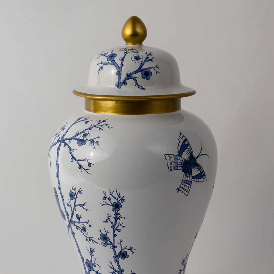 Closeup view of blue and white ceramic jar showing fine butterfly and branch artwork with glossy gold detailing.