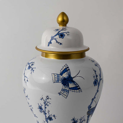 White ceramic jar with blue bird artwork and gold lid placed on white surface against neutral background enhancing traditional artistic home decor appeal.